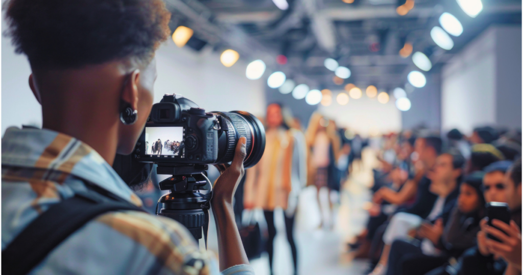 A male professional photographer taking photos on a camera at a fashion show.