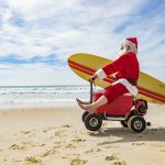 Santa Claus Doing a Wheelie on a Motorised Esky Cooler on the Beach