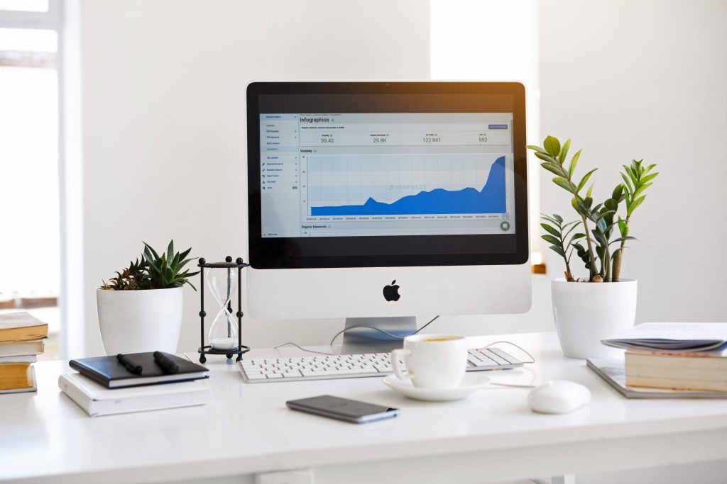 A computer on desk - in a room with data on screen