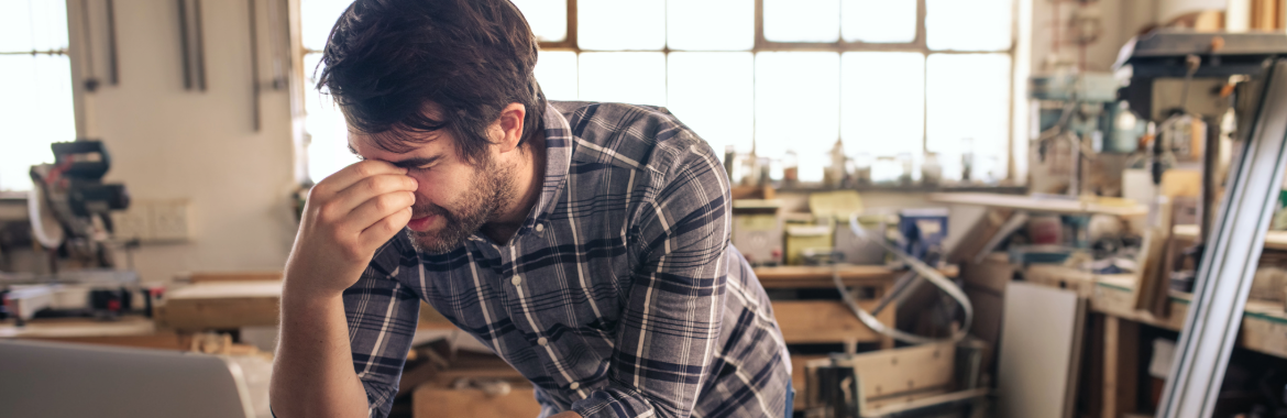 Overworked business owner in his carpentry work shed looking stressed and tired.