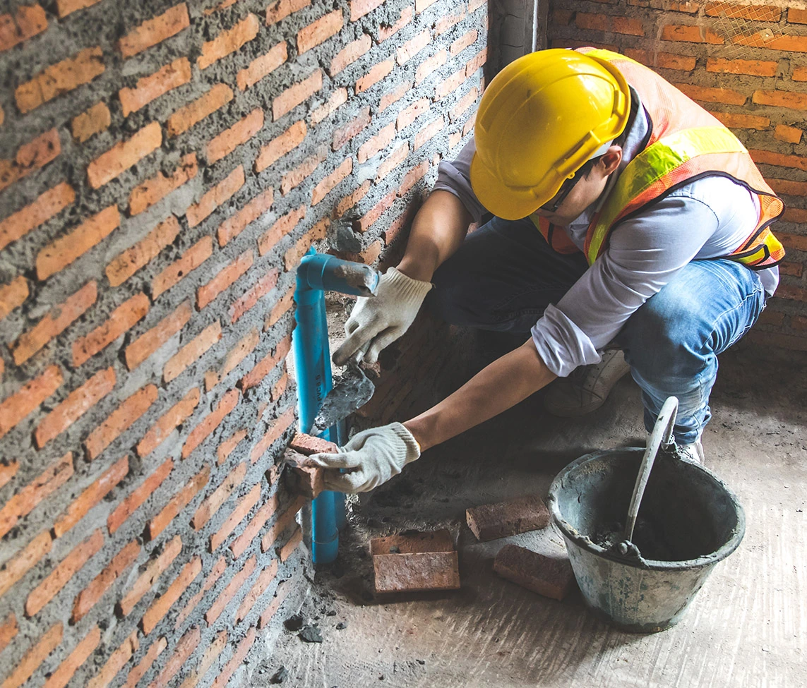 A bricklayer working building up brick wall with cement and tools