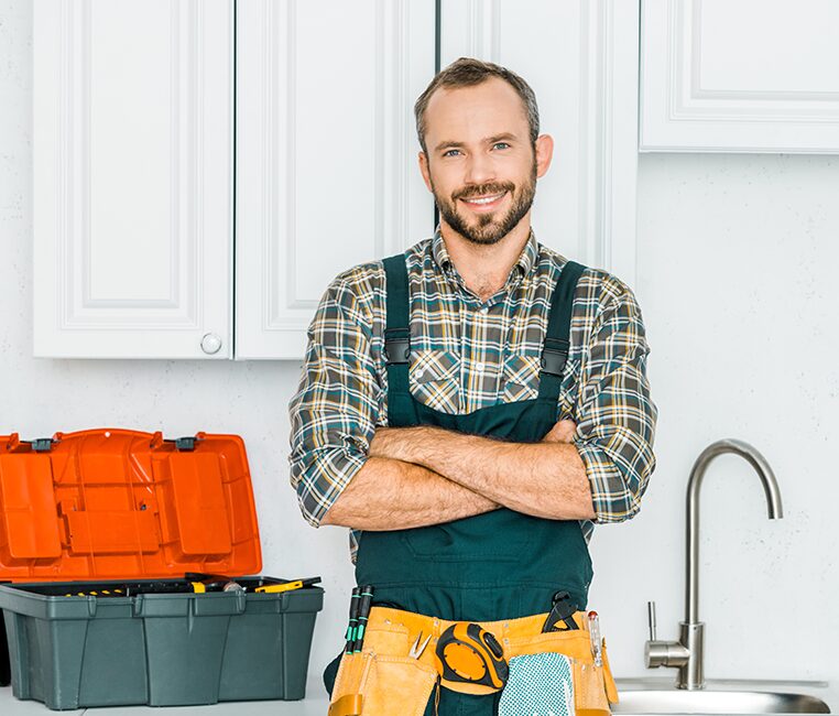 A smiling plumber stands in front of a kitchen sink
