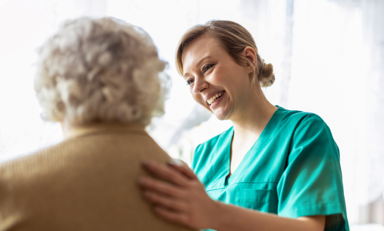 A smiling nurse interacts warmly with an older woman