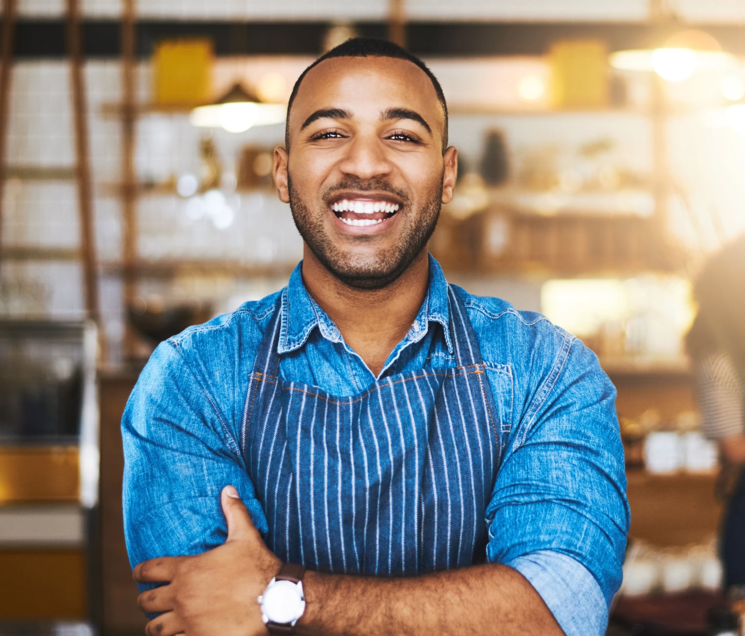 A cafe owner wearing an apron stands in a coffee shop