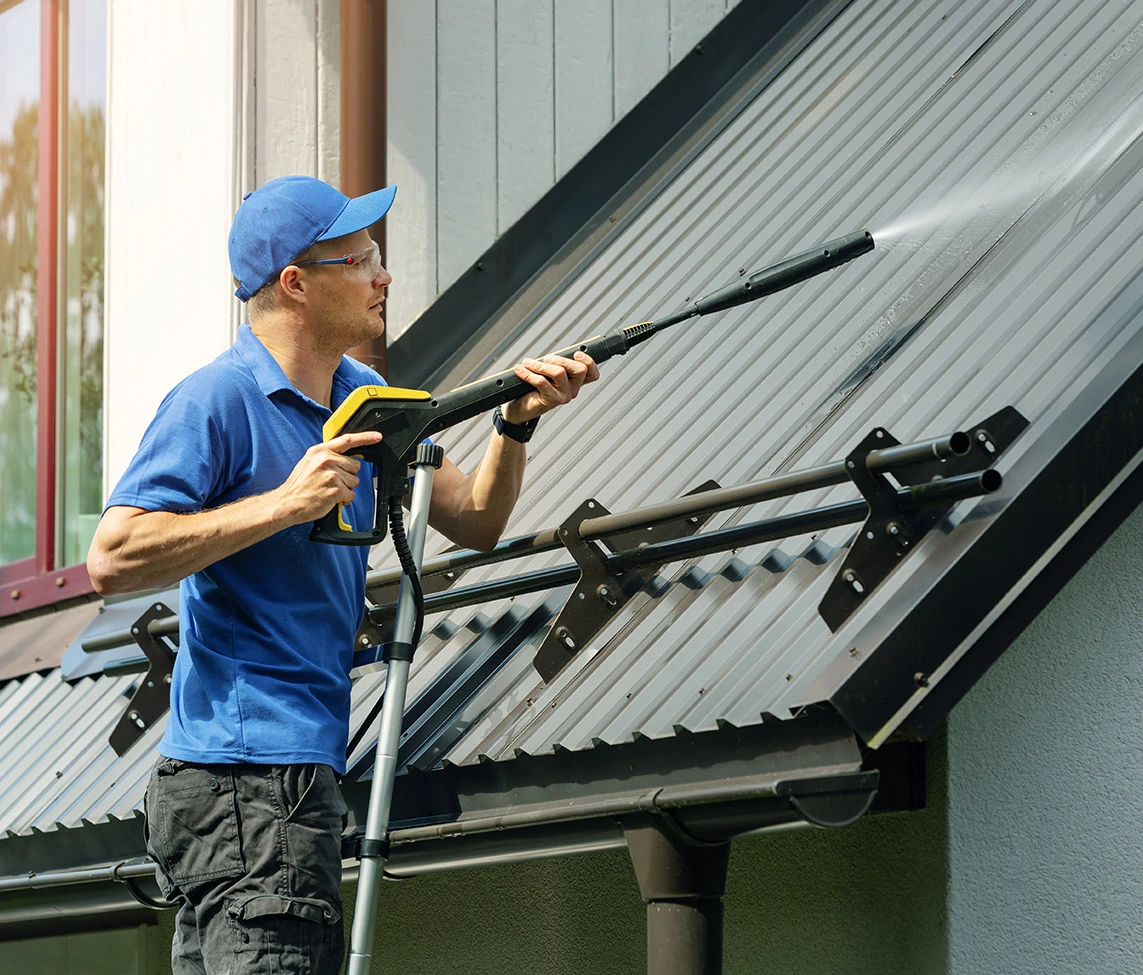 A pressure washer cleans the roof of a house
