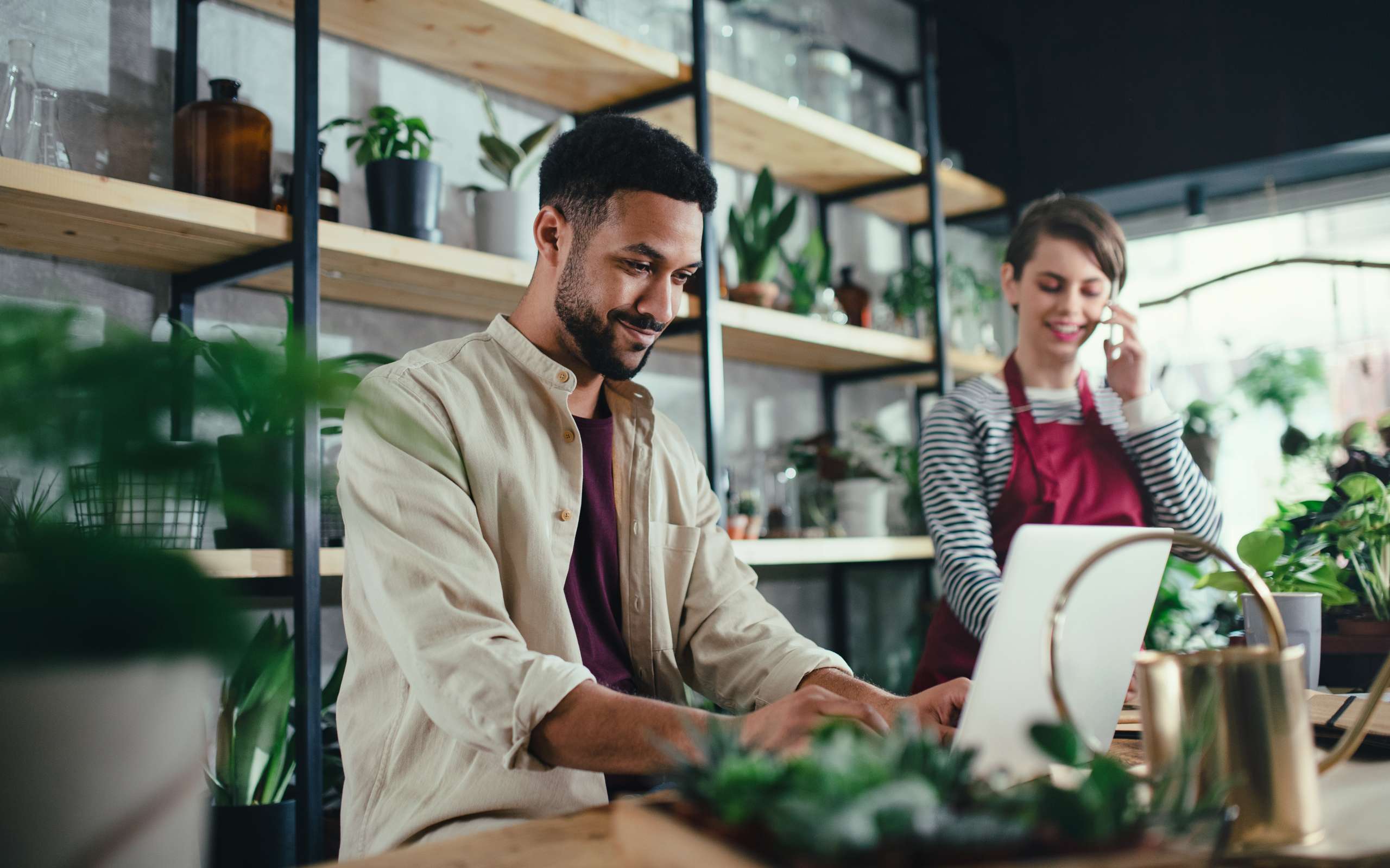 Man and woman shop assistants with laptop working in indoor potted plant store.