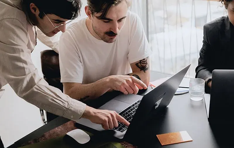 Two men collaborating over a laptop in a modern office setting, discussing business finance solutions and strategies