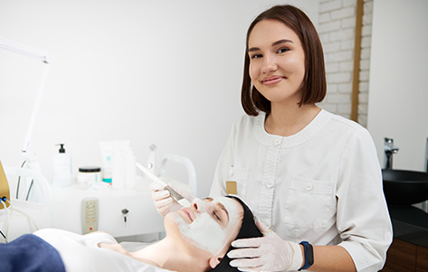 A beautician in a beauty salon applies a face mask, with salon tools and products.
